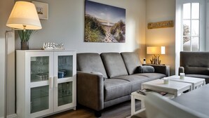 Ein modernes Wohnzimmer mit einem grauen Sofa, einer Glaskabine mit Weingläsern, einem Gemälde vom Strand und einem Schild mit der Aufschrift 'LORKIS LOKI'.