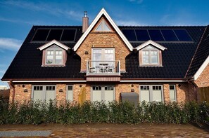 Uma casa de dois andares com fachada de tijolo, uma varanda e painéis solares no telhado.