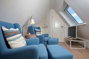 A modern living room with blue sofas, a round wooden table, a TV on a white stand, and a skylight above.