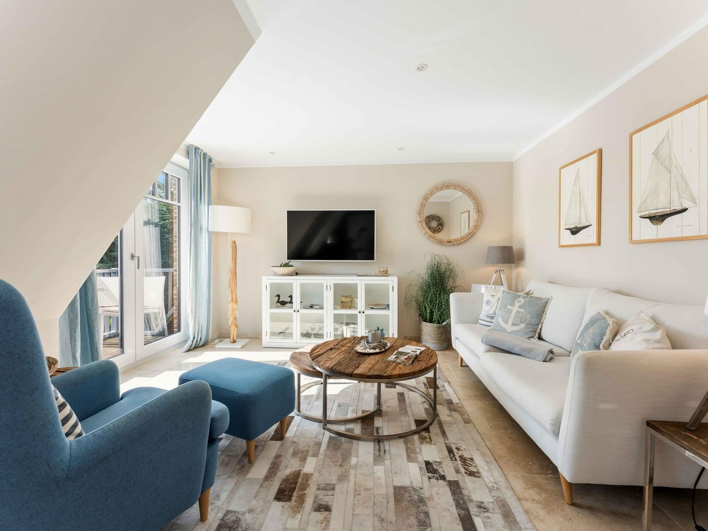Uma sala de estar moderna com um sofá branco, poltronas azuis, uma mesa de centro de madeira e uma televisão sobre um armário branco.