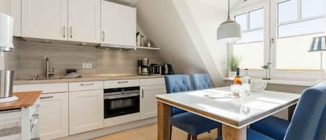 A modern kitchen with white cabinets, a built-in oven, and a dining area with a wooden table and blue chairs.