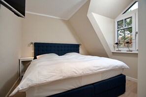 A bedroom with a bed, a nightstand, a window with a view of trees, and a sloped ceiling.
