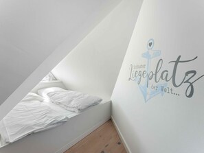 A room with a sloped ceiling, a bed with white bedding, and a wall with a logo and text. - Syltmuschel - Relaxen Sie in der Wunderschönen und Neuen 3-zimmerwohnung in Westerland (Sylt)
