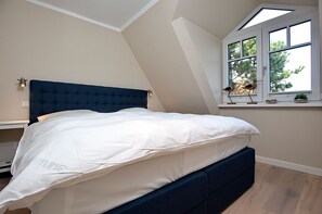 Quarto com cama, janela com vista para árvores e teto inclinado.
