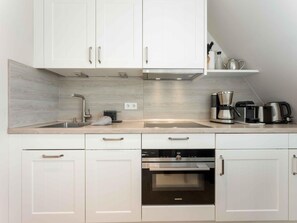Une cuisine moderne avec des meubles blancs, un évier en acier inoxydable, une machine à café et un four Siemens.