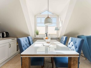 A modern kitchen with a white countertop, blue upholstered chairs, and a wooden table. - Syltmuschel - Relaxen Sie in der Wunderschönen und Neuen 3-zimmerwohnung in Westerland (Sylt)