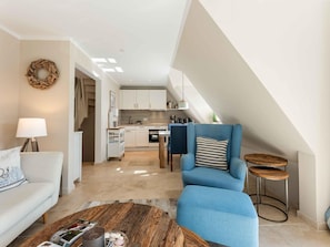 A modern living room with a sofa, a blue armchair, a coffee table, and a kitchen in the background.