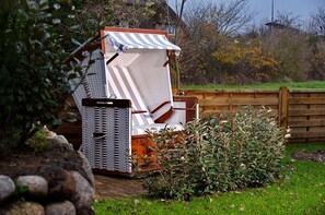 A beach chair with a striped awning, a wicker basket, and a wooden fence in the background. - Syltmuschel - Relaxen Sie in der Wunderschönen und Neuen 3-zimmerwohnung in Westerland (Sylt)