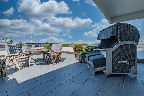 A rooftop terrace with a round table, two chairs, a grill, and potted plants.