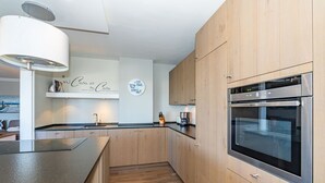 A modern kitchen with wooden cabinets, a built-in oven, and a pendant light. - Adlerhorst - Modern vacation apartment with large roof terrace and private sauna in (Sylt)