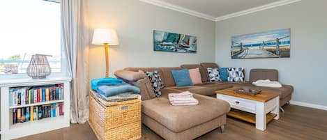 Una sala de estar acogedora con un sofá modular, una mesita de centro, una estantería y un ventanal con cortinas.