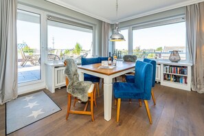 A dining area with a wooden table, blue chairs, and a view of the outdoors through large windows.