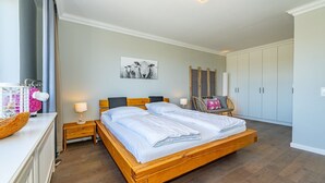 A bedroom with a wooden bed, bedside tables, a chair, and a wardrobe. - Adlerhorst - Modern vacation apartment with large roof terrace and private sauna in (Sylt)
