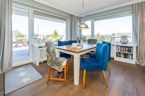 Un comedor con una mesa de madera, sillas azules y vistas al exterior a través de amplios ventanales.