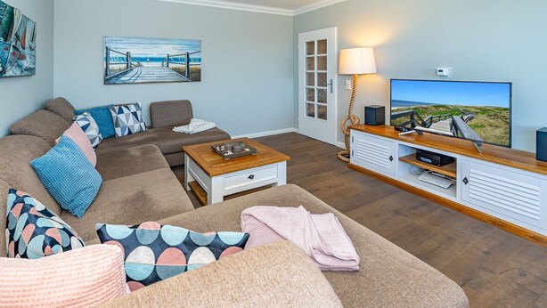 A living room with a sofa, coffee table, and TV stand. There is a painting on the wall and a door leading outside. - Adlerhorst - Modern vacation apartment with large roof terrace and private sauna in (Sylt)
