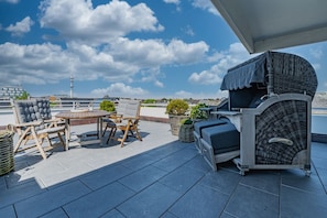 Une terrasse sur le toit avec une table ronde, deux chaises, un barbecue et des plantes en pot.