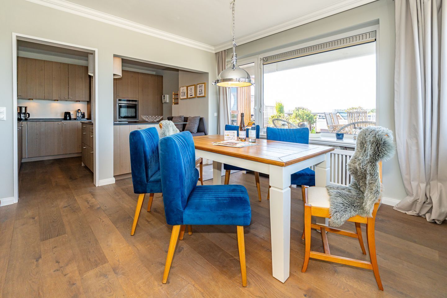 Eine moderne Küche mit Holzausbau, einem integrierten Backofen und einem Essbereich mit einem Holztisch und blau gepolsterten Stühlen.
