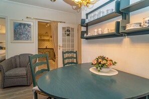 Un comedor con una mesa redonda, dos sillas, un jarrón de flores y estantes con objetos decorativos.