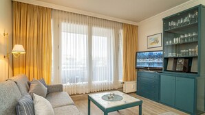 A living room with a sofa, coffee table, and a television. There is a cabinet with glassware and a picture on the wall. - App. Störtebeker App. 16 - Close to the beach & right in the city center. Vacation apartment for (Sylt)