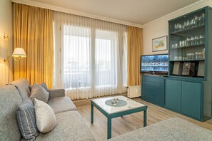 Sala de estar con sofá, mesa de centro y televisor. Se observa un aparador con cristalería y un cuadro en la pared.