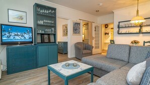A living room with a grey sofa, teal entertainment unit, and a television displaying birds. - App. Störtebeker App. 16 - Close to the beach & right in the city center. Vacation apartment for (Sylt)