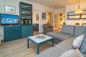 Ein Wohnzimmer mit grauem Sofa, einer türkisblauen Unterhaltungseinheit und einem Fernseher, der Vögel zeigt.