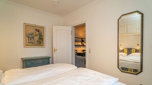 A bedroom with a large bed, a dresser, a painting, a mirror, and a door leading to a bathroom. - App. Störtebeker App. 16 - Close to the beach & right in the city center. Vacation apartment for (Sylt)
