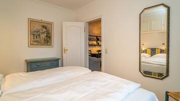Une chambre à coucher avec un grand lit, une commode, un tableau, un miroir et une porte donnant sur une salle de bain.