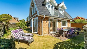 A two-story house with a patio area featuring outdoor furniture and a small table. - House Lotte - Holiday home for up to 6 people with garden. - only 450m to the (Sylt)