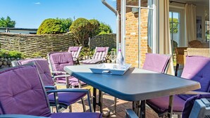 Eine Terrasse im Freien mit violetten Stühlen und einem Tisch, einer Steinmauer sowie Blick auf Bäume und ein Gebäude im Hintergrund.