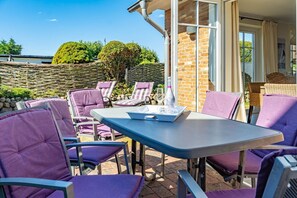 Eine Terrasse im Freien mit violetten Stühlen und einem Tisch, einer Steinmauer sowie Blick auf Bäume und ein Gebäude im Hintergrund.
