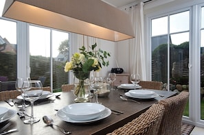 A dining table set with white plates, silverware, and wine glasses, surrounded by wicker chairs. A vase with flowers is placed on the table, and a radio is visible in the background. - House Lotte - Holiday home for up to 6 people with garden. - only 450m to the (Sylt)