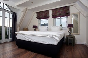 A bedroom with a large bed, two bedside tables, a window with curtains, and a view of the outside.