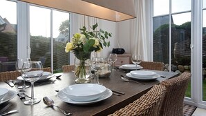 A dining table set with white plates, silverware, and wine glasses, surrounded by wicker chairs. A vase with flowers is placed on the table, and a radio is visible in the background. - House Lotte - Holiday home for up to 6 people with garden. - only 450m to the (Sylt)
