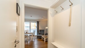 A hallway leading to a living area with a sofa, a table, and a lamp. There is a door with a coat rack and a picture frame on the wall.