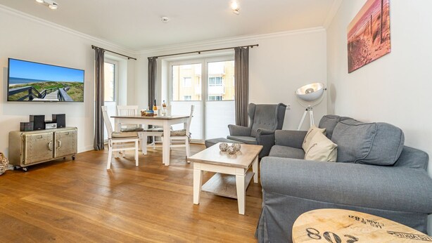 A modern living room with a grey sofa, a wooden coffee table, and a dining area with a white table and chairs.