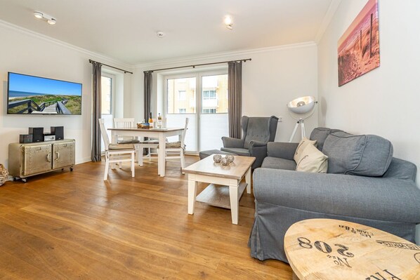 Una sala moderna con un sofá gris, una mesa de centro de madera y un comedor con una mesa y sillas blancas.