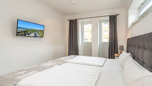 A hotel room with a bed, a TV mounted on the wall, and a window with curtains.