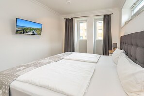Una habitación de hotel con una cama, un televisor montado en la pared y un ventanal con cortinas.