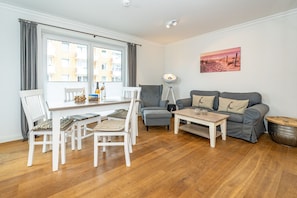 A modern living room with a dining area, a grey sofa, white chairs, a coffee table, and a painting on the wall.