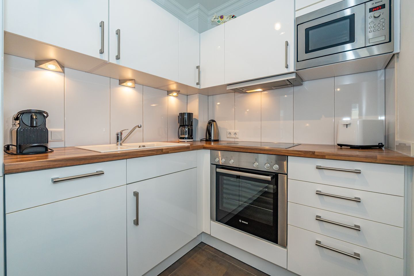 A modern kitchen with white cabinetry, a Bosch oven, a coffee maker, and a microwave.