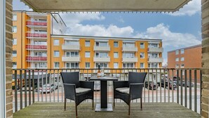 A balcony with two wicker chairs and a table, overlooking a multi-story building with orange and white tiles.
