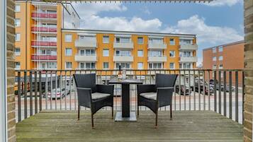 En balkon med to fletstole og et bord, med udsigt over en bygning med flere etager og orange og hvide fliser.