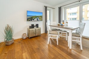 Un comedor con una mesa y sillas de madera, un televisor montado en la pared y vistas a un edificio por la ventana.