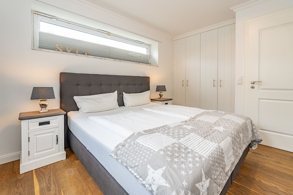 A bedroom with a large bed, two bedside tables with lamps, a wardrobe, and a mirror above the bed.