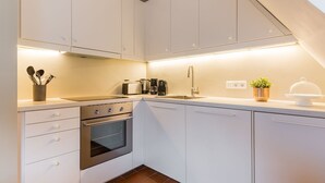 A modern kitchen with white cabinets, a stainless steel oven, and a countertop with a coffee maker and toaster. - Sönshörn Suite - 2-room vacation apartment on the Wadden Sea, in Munkmarsch. (Sylt)