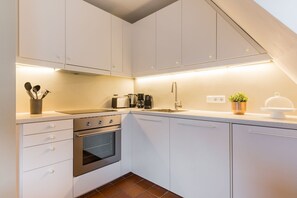 A modern kitchen with white cabinets, a stainless steel oven, and a countertop with a coffee maker and toaster.