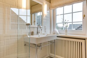 Un baño moderno con cabina de ducha de vidrio, un lavabo blanco y una ventana con vistas al exterior.