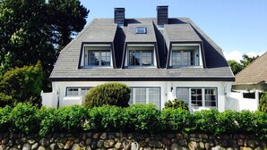 A two-story house with a stone wall in front, a large window on the ground floor, and a chimney on the roof. - Sönshörn Suite - 2-room vacation apartment on the Wadden Sea, in Munkmarsch. (Sylt)