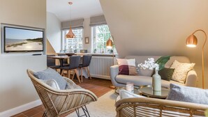 A modern living room with a sofa, chairs, a dining area, and a TV mounted on the wall. - Sönshörn Suite - 2-room vacation apartment on the Wadden Sea, in Munkmarsch. (Sylt)